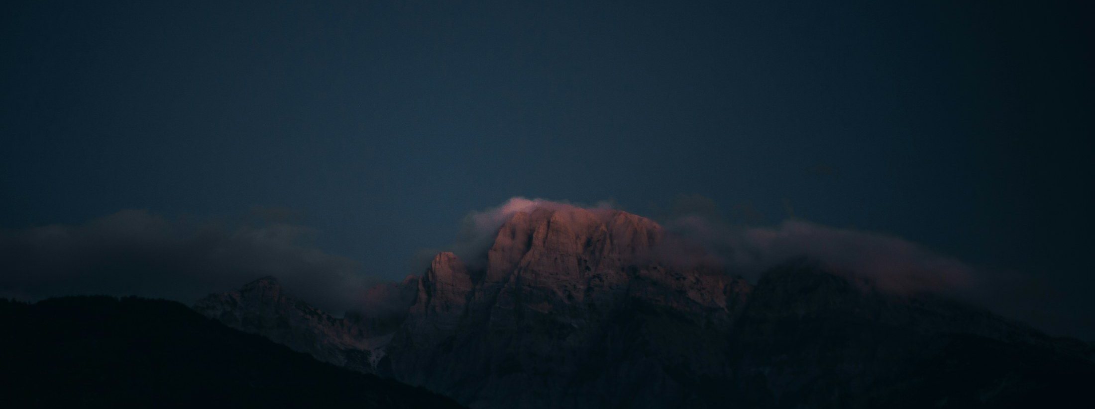 A dark mountain with its summit catching the last light